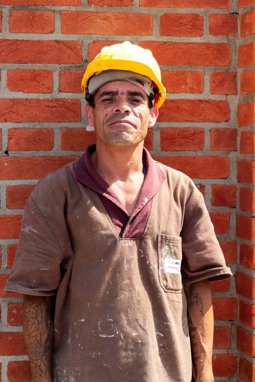 Portrait of a construction worker with hard hat standing against a brick wall outdoors.