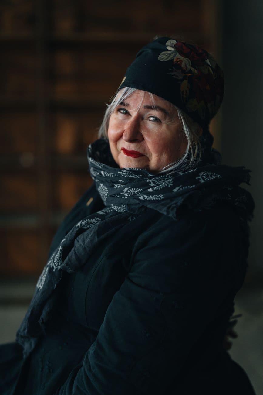 Charming portrait of an older woman in a floral scarf and hat, smiling warmly indoors.